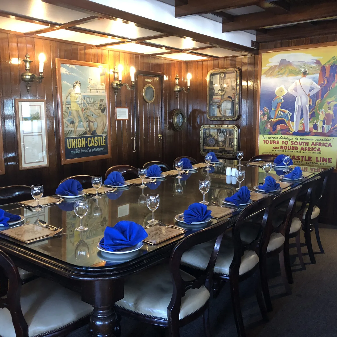 The Union-Castle private dining cabin, with wood panelling, vintage posters and a long table set with blue napkins