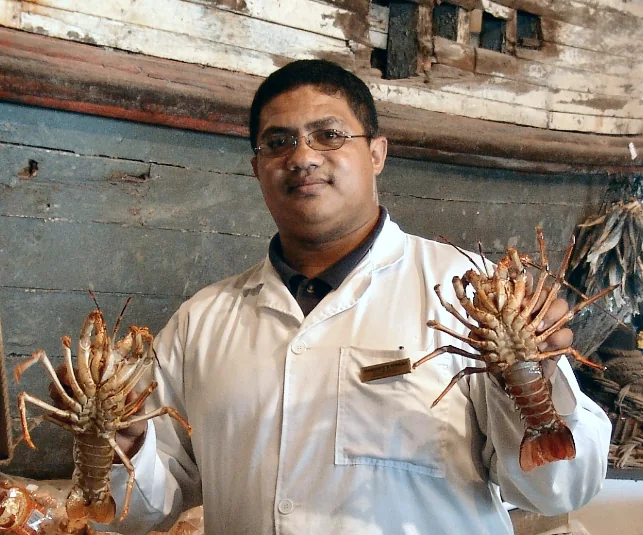 A fishmonger holding two live rock lobsters in front of the Kingfisher’s hull