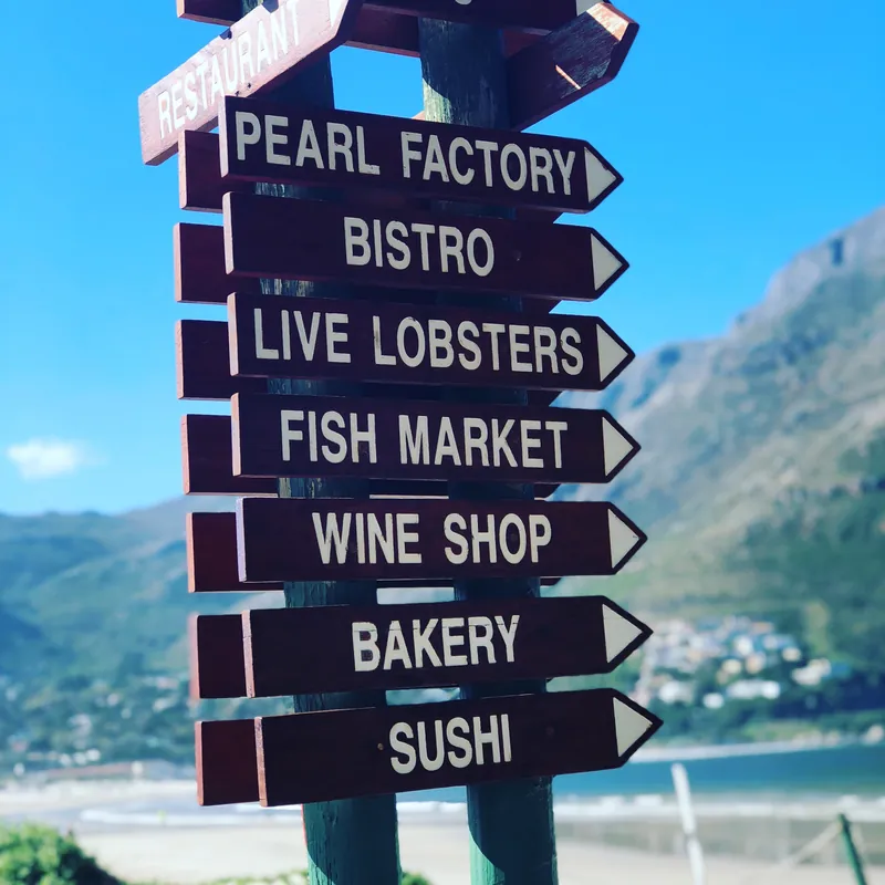 The real wooden signpost outside Mariner’s Wharf, pointing to the Pearl Factory, Bistro, Live Lobsters, Fish Market, Wine Shop, Bakery and Sushi